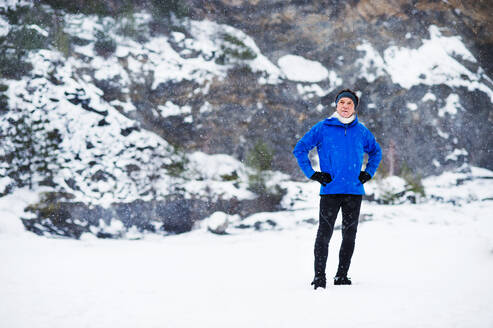 Ganzkörperporträt eines älteren Mannes, der nach dem Lauf in der winterlichen Natur steht, die Hände in die Hüften gestemmt. Kopierraum. - HPIF25434