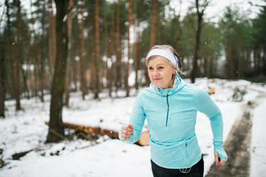 Ältere Frau joggt draußen in der winterlichen Natur. - HPIF25444