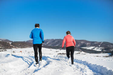 Rückansicht eines älteren Paares beim Joggen in verschneiter Winterlandschaft. - HPIF25452
