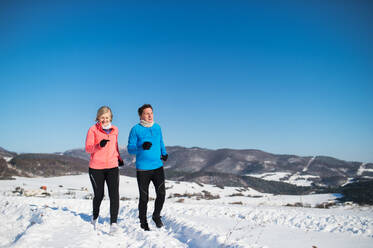 Älteres Paar joggt draußen in der winterlichen Natur. - HPIF25453