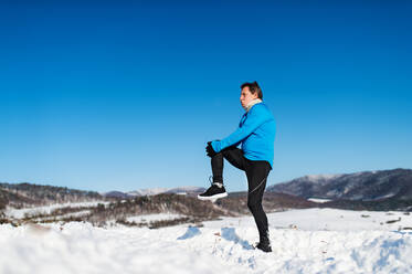 Älterer Mann, der sich vor dem Lauf in der winterlichen Natur die Beine ausstreckt, Kopierraum. - HPIF25459