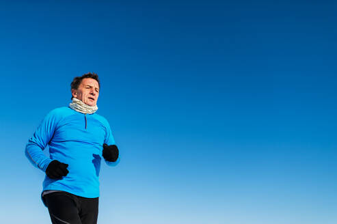 Älterer Mann joggt draußen in der winterlichen Natur, Raum kopieren. - HPIF25460