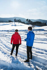 A rear view of senior couple runners standing in snowy winter nature, resting. - HPIF25472