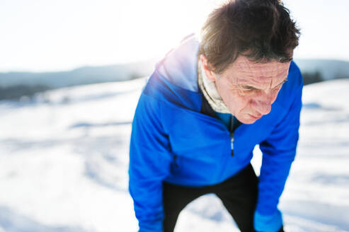 Ein Porträt eines älteren Mannes, der nach dem Lauf in der winterlichen Natur steht, die Hände auf den Knien, Kopierraum. - HPIF25476