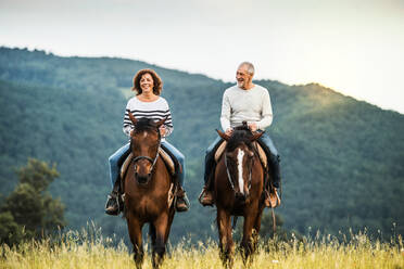 Ein glückliches älteres Paar reitet auf einer Wiese in der Natur. - HPIF25534