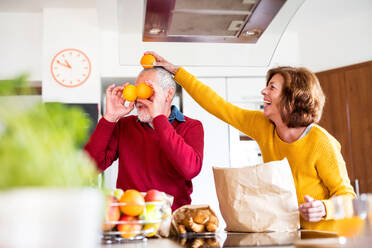 Ein älteres Ehepaar packt in der Küche Essen aus, ein alter Mann und eine alte Frau haben Spaß im Haus. - HPIF25543