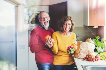 Senior couple unpacking food in the kitchen. An old man and woman inside the house. Shot through glass. - HPIF25549