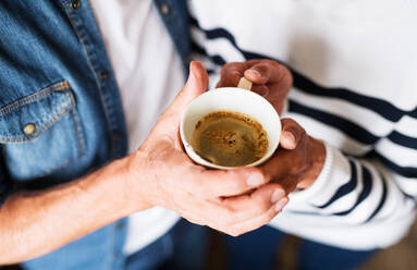 Unrecognizable senior couple at home. An old man and woman inside the house, holding a cup of coffee. Top view. - HPIF25561