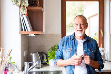 Ein älterer Mann in der Küche. Ein alter Mann im Haus, der eine Tasse Kaffee in der Hand hält. - HPIF25564