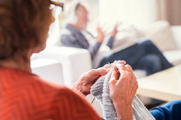 Unrecognizable senior couple relaxing at home. A woman knitting, and man listening to music in the background. - HPIF25573