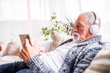 Älterer Mann mit Tablet und Kopfhörern, der sich zu Hause entspannt. Alter Mann hört Musik. - HPIF25576