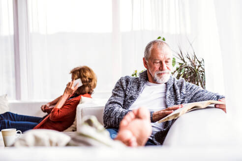 Glückliches älteres Paar mit Smartphone, das sich zu Hause entspannt. Eine Frau telefoniert und ein Mann liest ein Buch. - HPIF25582