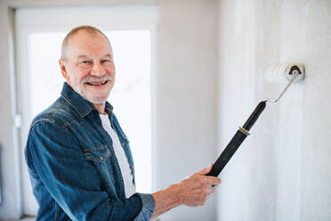 Porträt eines fröhlichen älteren Mannes, der in seinem neuen Haus die Wände streicht und Spaß hat - Konzept des Umzugs. - HPIF25611