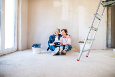 Glückliches älteres Ehepaar, das mit Hilfe eines Tablets die Wände in seiner neuen Wohnung streicht. Konzept des Umzugs. - HPIF25623