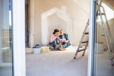 Happy senior couple painting walls in new home, using tablet. Relocation concept. - HPIF25631