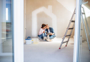 Happy senior couple with tablet painting walls in new home, kissing. Relocation concept. - HPIF25632