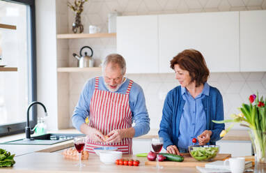 Ein Porträt eines glücklichen älteren Paares zu Hause beim Kochen. - HPIF25655