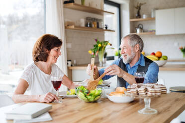 A senior couple in love having lunch indoors at home, talking. - HPIF25658