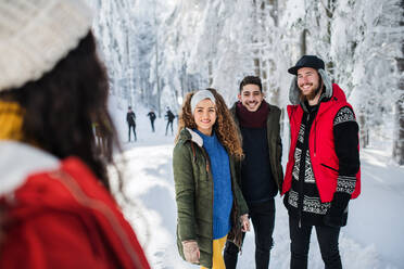 Eine Gruppe junger, fröhlicher Freunde, die im Winter im Schnee spazieren gehen und sich unterhalten. - HPIF25800