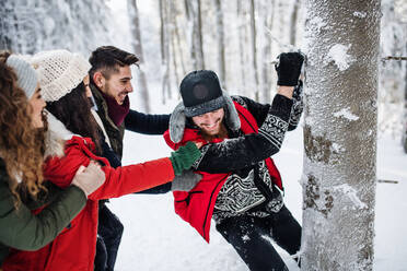 A group of young cheerful friends on a walk outdoors in snow in winter forest, having fun. - HPIF25804