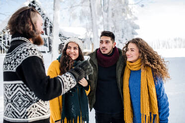 Eine Gruppe junger, fröhlicher Freunde, die im Winter im Schnee spazieren gehen und sich unterhalten. - HPIF25811