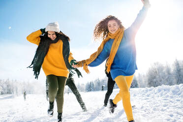 Eine Gruppe junger, fröhlicher Freunde auf einem Spaziergang im Schnee im Winterwald, die sich an den Händen halten und laufen. - HPIF25816