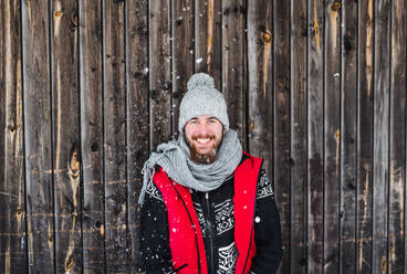 Porträt eines jungen Mannes in Vorderansicht vor einem hölzernen Hintergrund im Freien im Winter. - HPIF25824