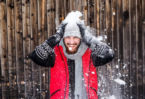 Porträt eines jungen Mannes, der im Winter im Freien vor einem hölzernen Hintergrund steht und Spaß hat. - HPIF25825