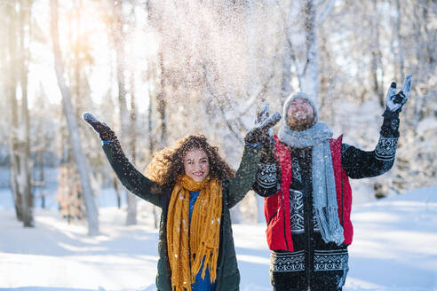 Ein Porträt eines Paares, das im Winterwald im Freien steht und Schnee wirft. - HPIF25835