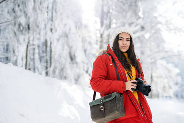 Eine junge Frau mit Kamera steht im Freien im Schnee im Winterwald. - HPIF25847