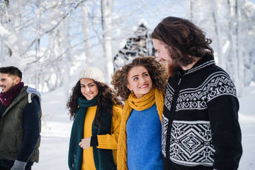 Eine Gruppe junger, fröhlicher Freunde, die im Winter im Schnee spazieren gehen und sich unterhalten. - HPIF25860