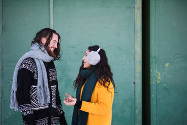 A side view portrait of young couple standing outdoors in winter, talking. - HPIF25885