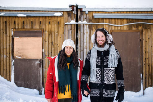 Ein Porträt eines jungen Paares, das im Winter im Freien steht und in die Kamera schaut. - HPIF25888