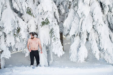 A portrait of topless young man outdoors in snow in winter forest, having fun. - HPIF25893