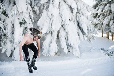 Ein Porträt von oben ohne jungen Mann im Freien im Schnee im Winter Wald, Spaß haben. - HPIF25894