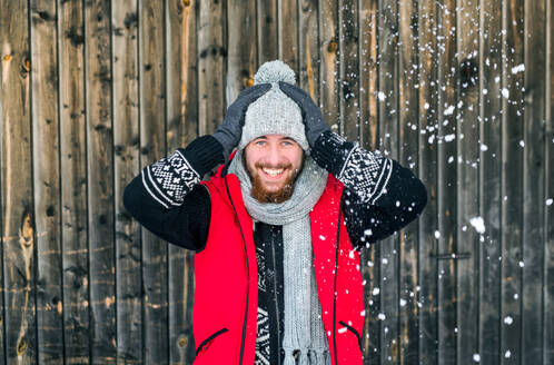 Porträt eines jungen Mannes in Vorderansicht vor einem hölzernen Hintergrund im Freien im Winter. - HPIF25901