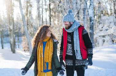 Ein Porträt eines Paares, das im Schnee im Winterwald spazieren geht und sich unterhält. - HPIF25913