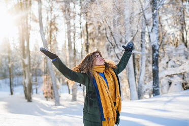 Porträt einer jungen Frau, die im verschneiten Winterwald im Freien steht und Schnee wirft. - HPIF25914