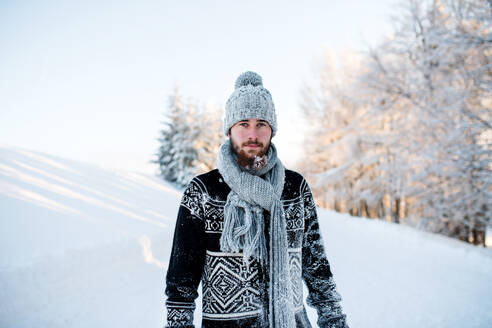 Porträt eines jungen Mannes, der im Winter in der Natur im Schnee steht und in die Kamera schaut. - HPIF25924