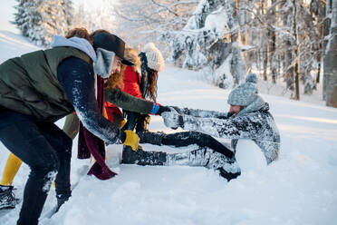 Eine Gruppe junger, fröhlicher Freunde auf einem Spaziergang im Schnee im Winterwald, die Spaß haben. - HPIF25928