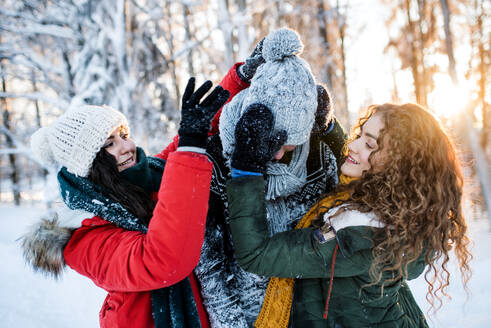 Eine Gruppe fröhlicher junger Freunde, die draußen im Schnee im Winterwald stehen und Spaß haben. - HPIF25931