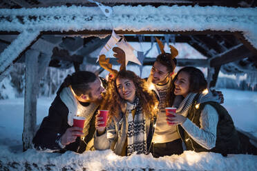 A group of young friends outdoors in snow in winter at night, holding drinks. - HPIF25939