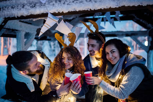 A group of young friends outdoors in snow in winter at night, holding drinks. - HPIF25941