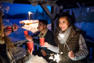 A group of young friends outdoors in snow in winter at night, holding sparklers. - HPIF25948