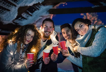 A group of young friends outdoors in snow in winter at night, holding drinks. - HPIF25949