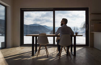 A rear view of mature man sitting at the table in new home, using tablet. - HPIF25982