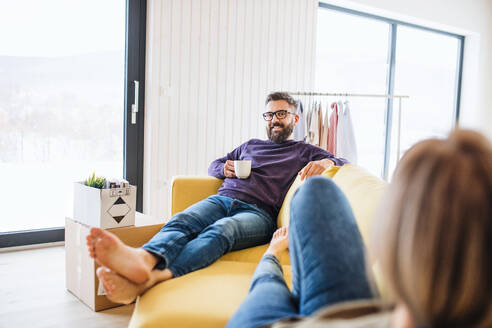 Ein junges Paar sitzt mit einer Tasse Kaffee auf dem Sofa und zieht in ein neues Haus ein. - HPIF26008