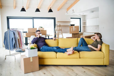 Ein junges Paar sitzt mit einer Tasse Kaffee auf dem Sofa und zieht in ein neues Haus ein. - HPIF26009