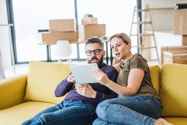 Ein glückliches junges Paar mit Tablet auf dem Sofa sitzend, das in ein neues Haus einzieht. - HPIF26010