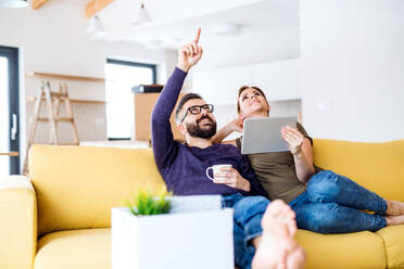 Ein glückliches junges Paar mit Tablet auf dem Sofa sitzend, das in ein neues Haus einzieht. - HPIF26011